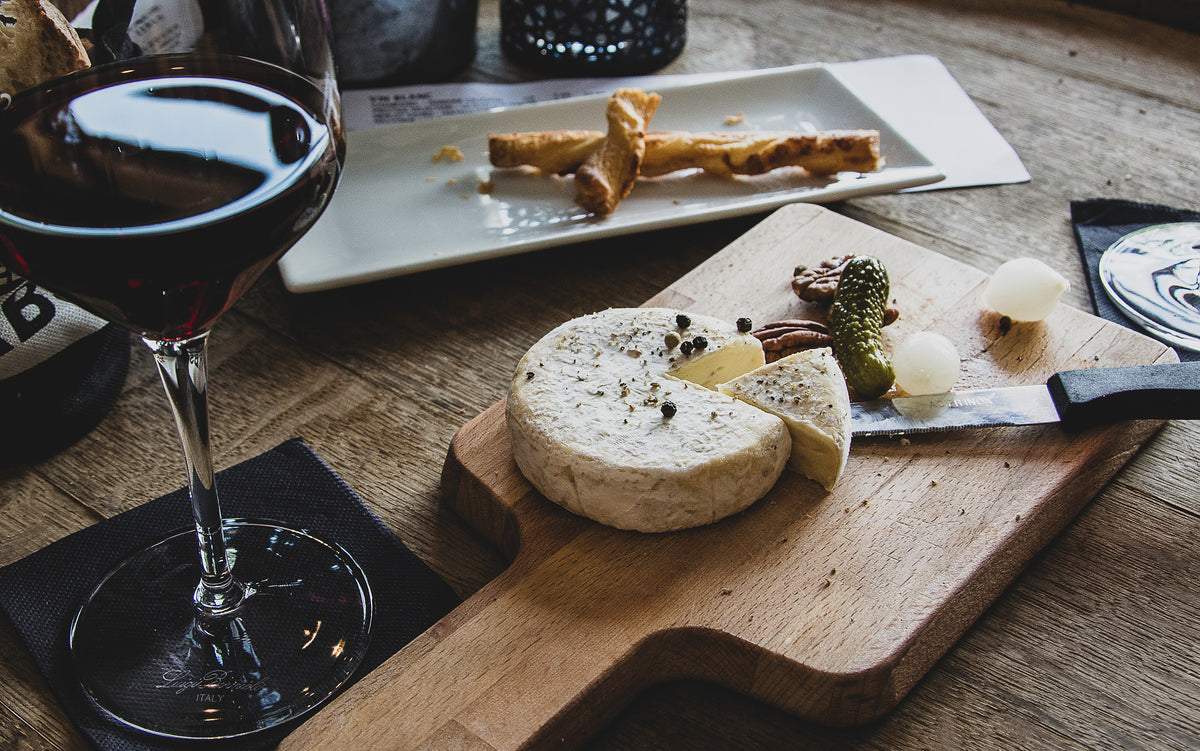 Käseplatte mit Weichkäse, Gebäck und einem Glas Rotwein